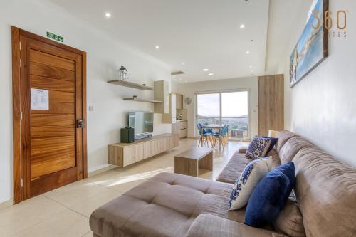 ein Wohnzimmer mit einem braunen Sofa und einer Küche in der Unterkunft Spacious, designer 2BR home with Captivating Views by 360 Estates in Mellieħa
