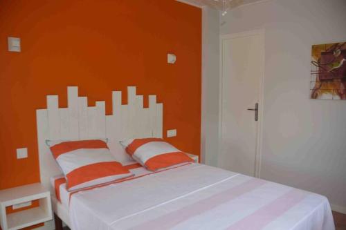 a bedroom with a white bed with an orange wall at kaï colibri in Rivière-Pilote