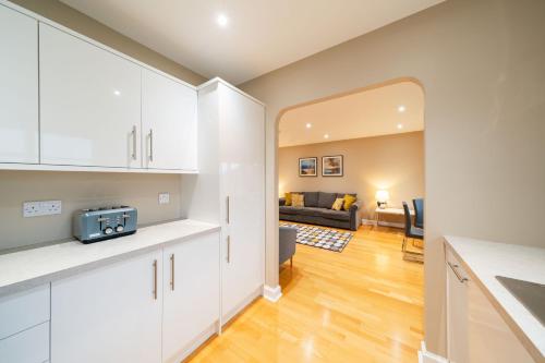 a kitchen with white cabinets and a living room at Strathallan - Luxury 3 Bedroom Apartment, Gleneagles, Auchterarder in Auchterarder