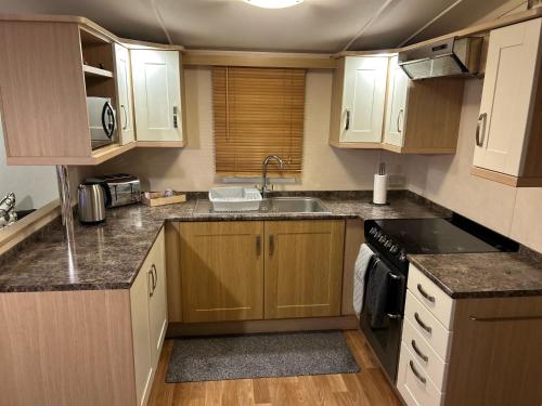 a small kitchen with wooden cabinets and a sink at Great Caravan On A Family Holiday Park In Essex, Ref 37055g in Clacton-on-Sea