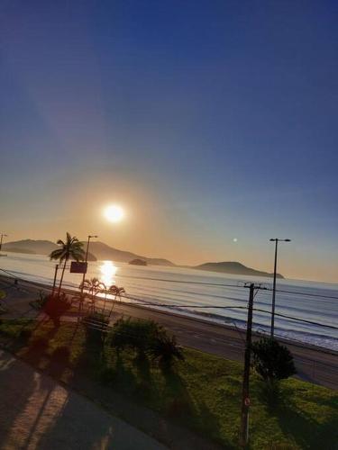 a sunset on a beach with the sun rising over the ocean at Ap Vista Mar em Caraguatatuba in Caraguatatuba