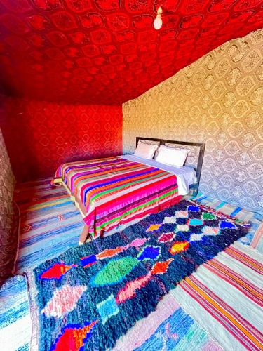 a bedroom with a bed and a colorful rug at Mhamid Sahara Camp Activities - Le Chant du Sable in Mhamid