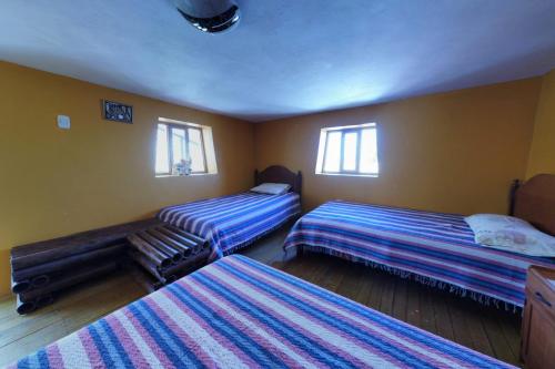 a bedroom with two beds and two windows at KanchayKillaWasi in Chinchero