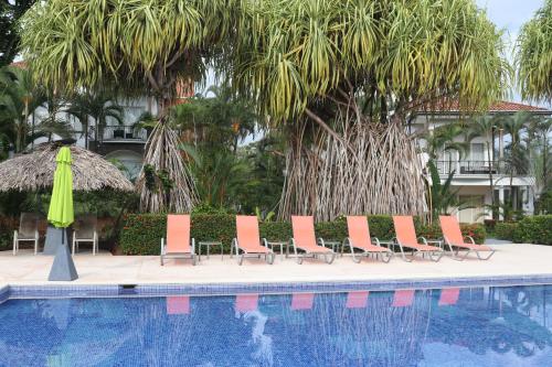 a group of chairs and a pool with a umbrella and trees at Del Pacifico Condo C7 in Bejuco