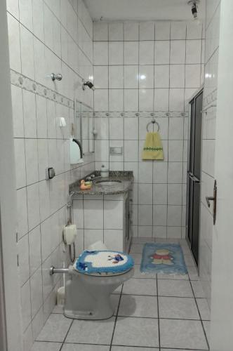 a white tiled bathroom with a toilet and a sink at CASA de 2 QUARTOS in Guaratinguetá