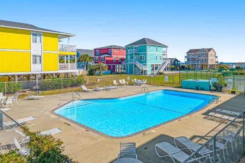a swimming pool with chairs and houses in the background at Captain's Villa 9-C Sunshine Ally in Holden Beach