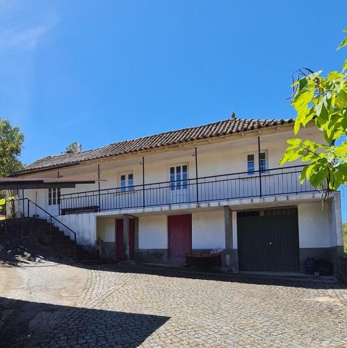 a white building with red doors and a balcony at Casa de Cabecinho- Albufeira do Azibo in Bragança