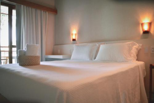 a bedroom with a large bed with white sheets and pillows at AL MAR SUÍTES in Praia do Forte