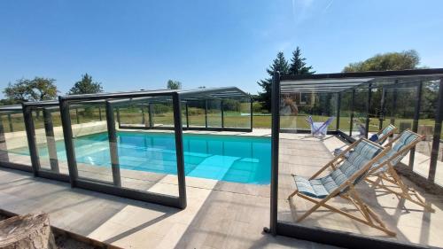 une maison en verre avec une piscine et deux chaises dans l'établissement Nature et Hotes, à Quiers-sur-Bézonde