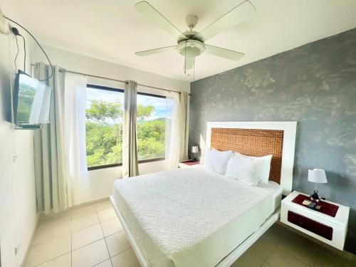 een slaapkamer met een bed, een plafondventilator en een raam bij Tropical Gardens Suites and Apartments in Coco