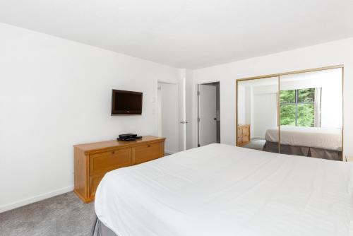 a white bedroom with a bed and a television at The Woodrun Lodge by Whiski Jack in Whistler