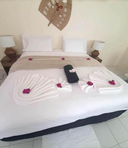 uma cama com lençóis brancos e flores cor-de-rosa em Wolfgramm Beachfront Motel em Utungake