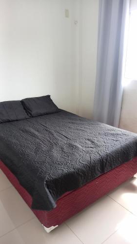 a bed with a black comforter on top of it at Apartamento inteiro in Serra