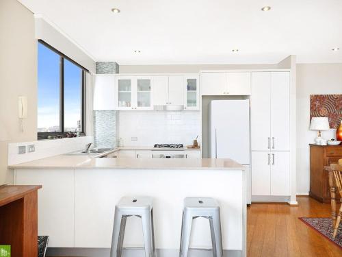 a kitchen with white cabinets and a large island with stools at It's Paradise Here, Private Room with Breakfast and 2 cats in Wollongong
