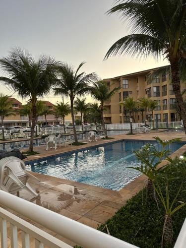 a swimming pool with palm trees and a resort at Loft no Condomínio Reserva do Sahy + Piscina in Mangaratiba