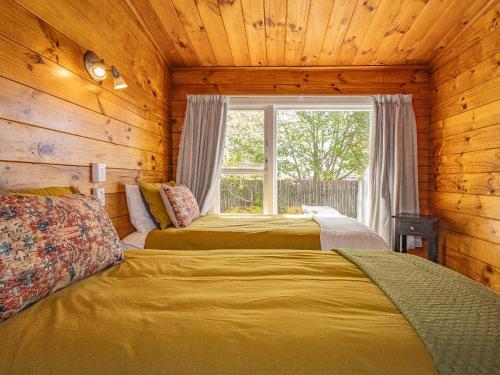two beds in a log cabin with a window at Kaka Retreat - Taupo Holiday Home in Taupo
