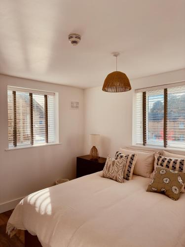 a bedroom with a white bed with pillows and windows at Chic Barn Conversion in the Cotwolds in Enstone