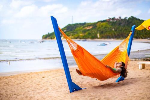 a woman laying in a hammock on a beach at Sol do Caribe Suítes in Maragogi