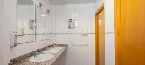 Baño con 3 lavabos y espejos en la pared en Mellow Barcelona en José Galves