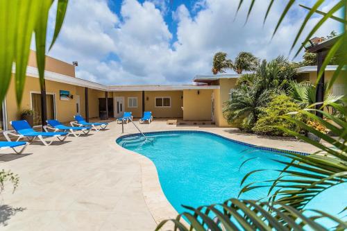 a swimming pool in front of a house with blue lounge chairs at Juanedu Suites in Oranjestad