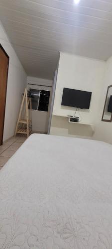 um quarto com uma cama branca e uma televisão de ecrã plano em Linda Kitnet Mobiliada Mar Itapua em Vila Velha
