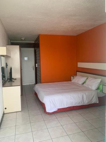 a bedroom with a large bed with an orange wall at Paisible studio in Les Trois-Îlets