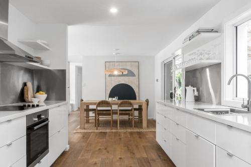 a kitchen with white cabinets and a dining table at Pool House - Peaceful Luxury, Byron Bay in Byron Bay