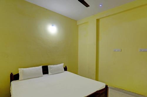 um quarto com uma cama branca e paredes amarelas em OYO Hotel RS Guest House em Katni