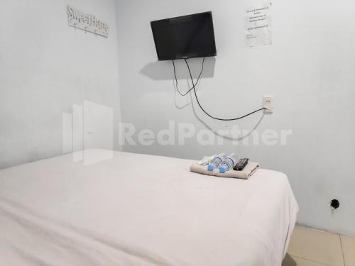 a white room with a bed with a tv on the wall at Ada Guest House Medan Redpartner in Medan