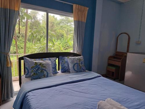 a bedroom with a bed with blue sheets and a window at Dr. House in Khao Kho