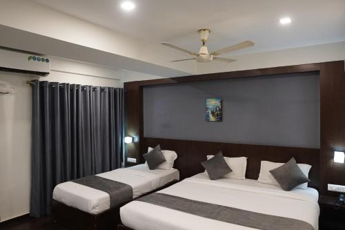 two beds in a hotel room with a ceiling fan at Luciya International Mysore in Mysore