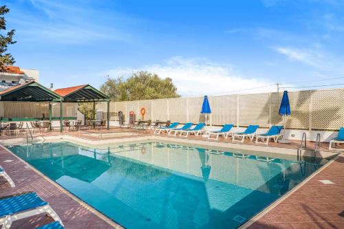 a swimming pool with chairs and blue umbrellas at Paradise Hotel-Apartments in Stalida