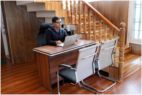 a man sitting at a desk with a laptop at White House Cottage in Kolur