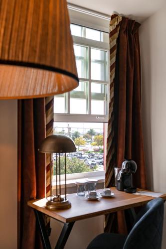 a desk with a lamp in front of a window at Dona Maria Hotel in Figueira da Foz