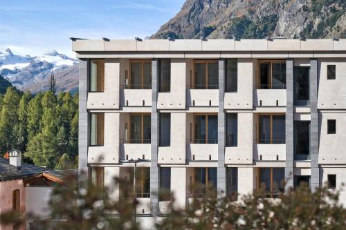 a white building with windows and mountains in the background at Hotel Maistra 160 in Pontresina