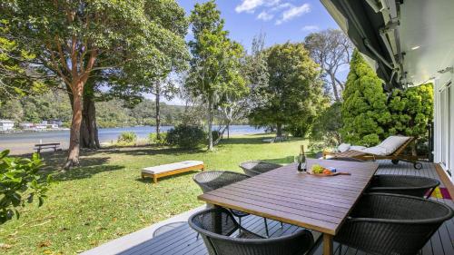 einen Holztisch und Stühle auf einer Veranda mit Blick auf das Wasser in der Unterkunft The Patonga Pearl in Patonga