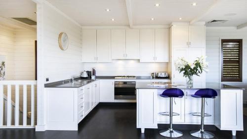 a white kitchen with white cabinets and purple stools at A Grand Beach Retreat in Killcare