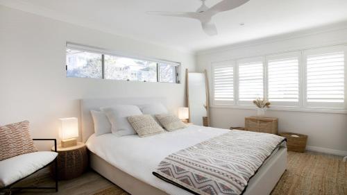 a white bedroom with a bed and two windows at Beach Vibes at Terrigal in Terrigal