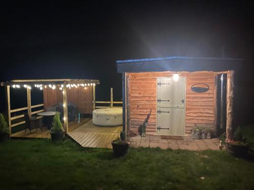 um barracão de madeira com uma banheira num quintal à noite em The original Sleeping Giant Lodge - Farm Stay, meet the animals em Ystradgynlais