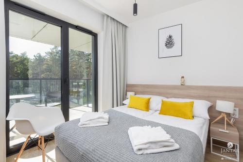 a bedroom with a bed with yellow pillows and a balcony at Shellter Apartments 117 H - by Jantar Apartamenty in Rogowo