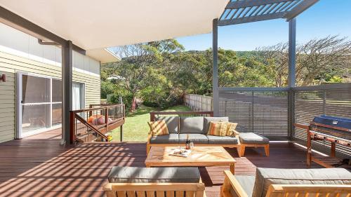 Un patio con un sofá y una mesa en una terraza. en Killcare Beach Abode with AC, en Killcare