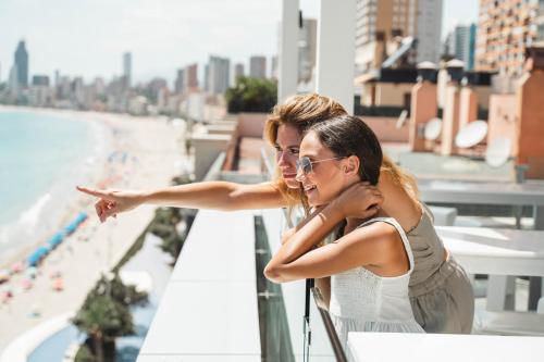 dwie kobiety stojące na balkonie z widokiem na plażę w obiekcie Hotel Villa del Mar w mieście Benidorm