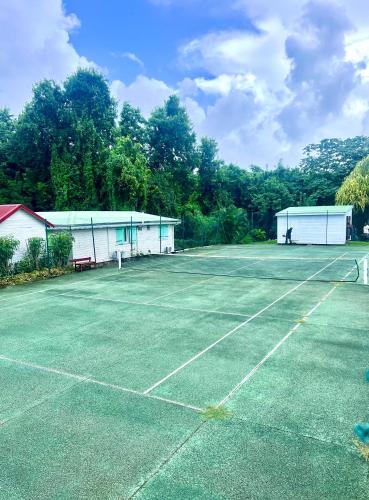 a tennis court with two white buildings and trees at cœur d hibiscus P&V in Sainte-Luce