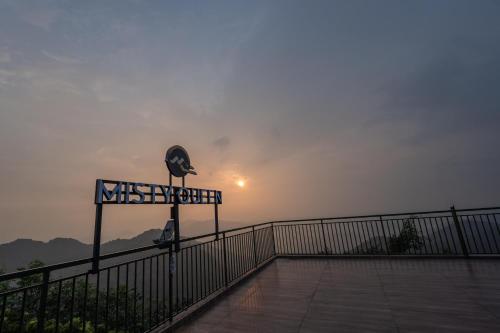 a sign on a bridge with the sun in the background at Misty Queen By Dimora Hotels in Kakkadampoyil