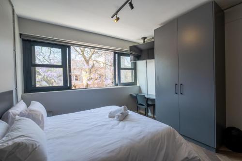 1 dormitorio con cama blanca y ventana en Inn & Out Plus Rosebank en Johannesburgo