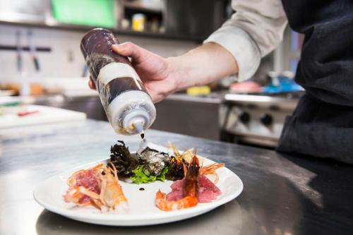 a person is pouring food onto a plate of food at Hotel Del Porto in Torri del Benaco