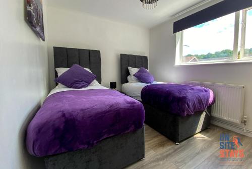 1 Schlafzimmer mit 2 Betten mit violetter Bettwäsche und einem Fenster in der Unterkunft OnSiteStays - Ideal Long Term Retreat, 2-BR House with Conservatory, Parking & Wi-Fi in Canterbury