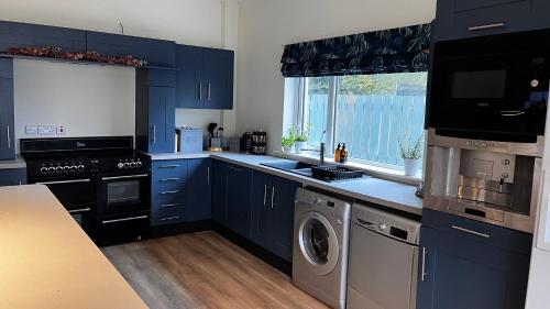 uma cozinha com armários azuis e uma máquina de lavar e secar roupa em Lisnevenagh Cottage em Ballymena