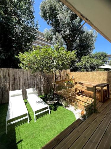 un jardin avec deux chaises blanches et une terrasse en bois dans l'établissement Appartement avec jardin proche mer, à Antibes