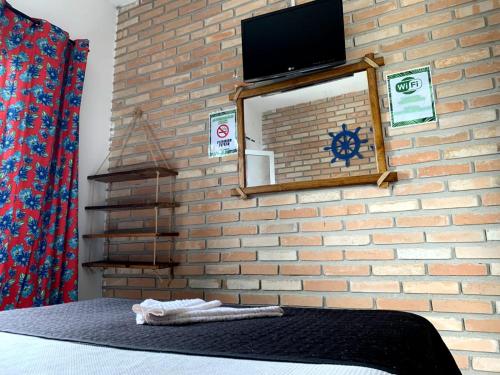 a bedroom with a brick wall with a mirror and a tv at Hostel Vento Leste in Bombinhas